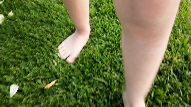Feet of little girl while walking on grass in park or garden