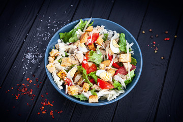View from above Caesar salad with chicken, lettuce, parmesan cheese, tomato. Copy space for design. Healthy food bowl. Dieting. bowl on dark wooden background. healthy and balanced food