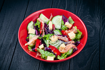 Close up view on fresh homemade salad with salmon, tomato, cucumber, lettuce and cheese. Healthy food. Seafood for lunch. Copy space. Salad bowl on dark background. Green salad