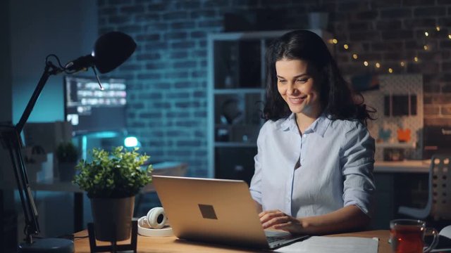 Happy businesswoman attractive girl is working in office late at night using computer smiling enjoying work. People, workaholism and business concept.