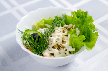 boiled chicken salad with squid, pickled cucumbers, mayonnaise, carrots, lettuce, greens and olive in white dish