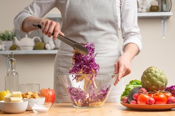 The chef mixes the salad, stir, in the process of a vegetarian salad in the home kitchen. Light background for restaurant menu design, menu, recipe book. Healthy food, detox