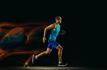 Professional male runner training isolated on black studio background in mixed light. Man in...
