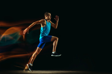 Fototapeta na wymiar Professional male runner training isolated on black studio background in mixed light. Man in sportsuit practicing in run or jogging. Healthy lifestyle, sport, workout, motion and action concept.