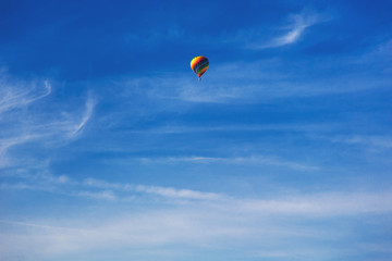 Balloon flying through the blue sky among the clouds. Freedom, adventure, loneliness.