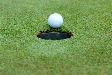 White Golf ball on green course near hole on blurred landscape of golf course in bright day time with copy space. Sport, Recreation, Relax in holiday concept