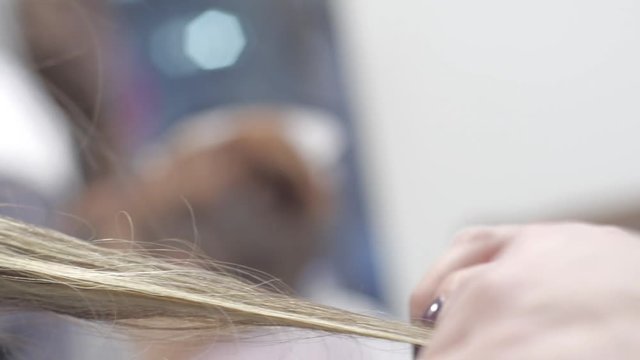 Haidresser using flat iron straightener on female customer hair in salon close up