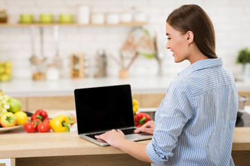 Woman searching recipes online on laptop with blank screen