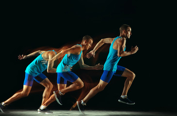 Fototapeta na wymiar Professional male runner training isolated on black studio background in mixed light. Man in sportsuit practicing in run or jogging. Healthy lifestyle, sport, workout, motion and action concept.