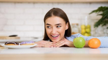 Woman choosing between fruits and sweets, looking at donut