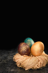 Easter dyed eggs on dark background. Luster shiny golden color eggs in a nest