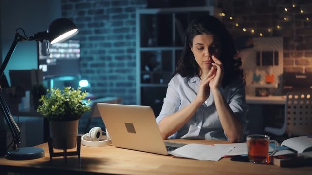 Stressed tired girl is working at night in office reading documents suffering from headache touching head sitting at desk in office. People and workaholism concept.