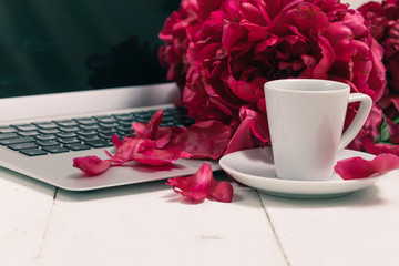 Home office desk with laptop, pink peonies, mug of coffee, stationery, glasses on a white background