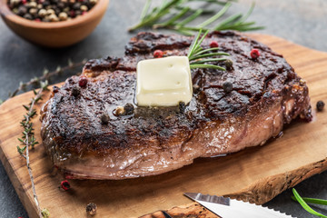 Medium rare Ribeye steak with herbs and a piece of butter on the wooden tray.