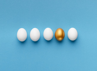 Golden egg lying between white ones on blue background