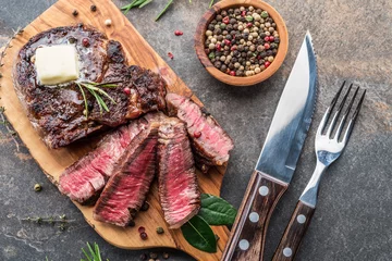 Poster Medium rare Ribeye steak with herbs and a piece of butter on the wooden tray. © volff