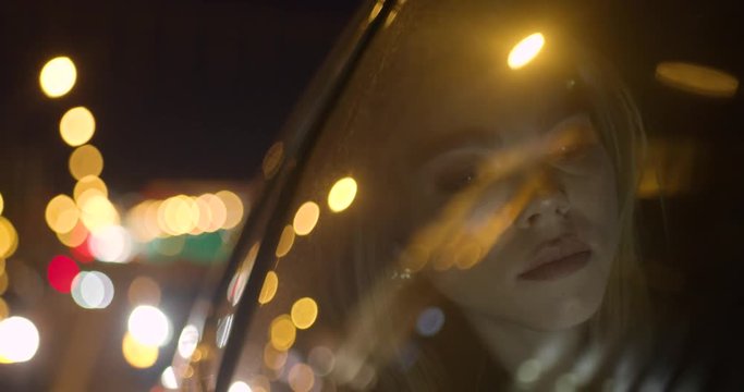 Young girl uses a smartphone, sitting on back seat of a car, night road in the city, reflection of lights in glass.