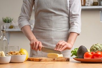The chef cuts mozzarella cheese or feta, stir, in the process of a vegetarian salad in the home kitchen. Light background. restaurant menu, menu, recipe book. Healthy food, detox