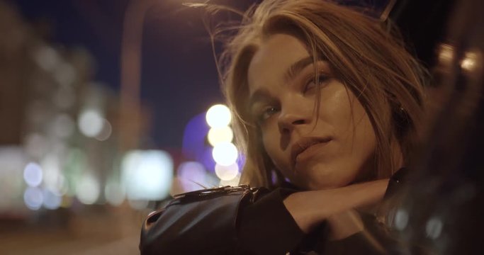 Young girl in car, leans out passenger side car window, wind stirs her hair, she looks at the night city, night road.