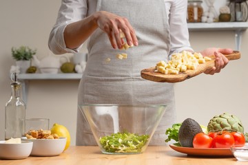 Cooking. A chef pours mozzarella or feta cheese, in the process of a vegetarian salad in the home kitchen. Light background. Restaurant menu, menu, recipe book. Healthy nutrition, detox