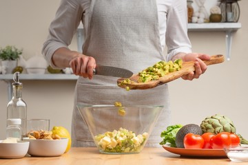 Cooking. The chef pours avocado, in the process of a vegetarian salad in the home kitchen. Light background. Restaurant menu, menu, recipe book. Healthy nutrition, detox