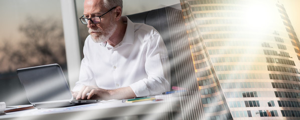 Senior businessman working on laptop in office, hard light; multiple exposure