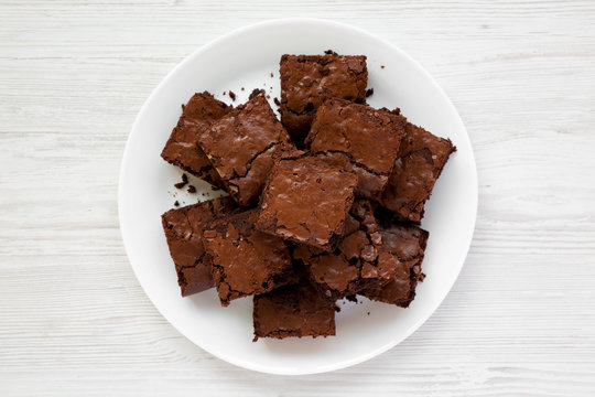 Homemade chocolate brownies on a white plate on a white wooden surface, top view. Flat lay, overhead, from above. Close-up.