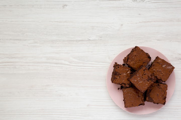 Homemade chocolate brownies on a pink plate on a white wooden background, top view. Flat lay,...