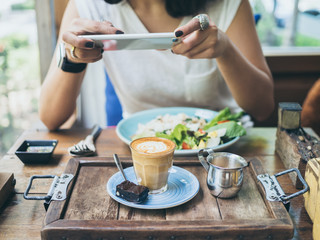 Woman's hands taking photo of coffee cup on wooden table by smartphone
