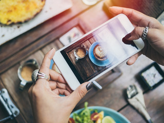 Woman's hands taking photo of coffee cup on wooden table by smartphone