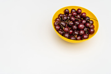 Ripe juicy red cherries in a yellow bowl in the upper-right corner of white table. Vitamin healthy food for a healthy lifestyle. 