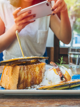 Woman's hands taking photo of the dessert on wooden table by smartphone