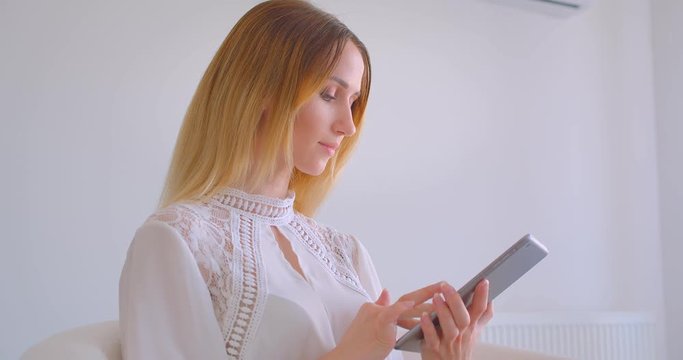 Closeup portrait of young pretty caucasian businesswoman using the tablet looking at camera in a white room