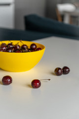 Close-up. Ripe juicy red cherries in a yellow bowl on a white tablein the kitchen. Vitamin healthy food for a healthy lifestyle. Vertical
