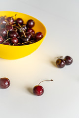 Close-up. Ripe juicy red cherries in a yellow bowl on a white table. Vitamin healthy food for a healthy lifestyle. Vertical