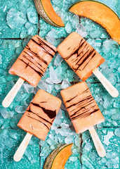 Fruit homemade popsicles with slices of fresh cantaloupe melon and ice cubes on light rustic turquoise background. Top view.