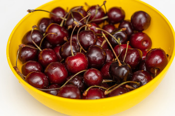 Close-up. Ripe juicy red cherries in a yellow bowl on a white table. Vitamin healthy food for a healthy lifestyle