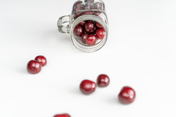 Red juicy cherries scattered from out the glass jar on a white table