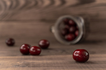 Red juicy cherries scattered from the blurred glass jar on a wooden table
