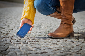 Woman picking up broken smartphone from street