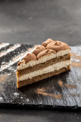 Slice of tiramisu cake on stone board on black background