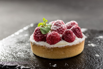 Raspberry tartlets with icing sugar close up on stone board on black background - Powered by Adobe