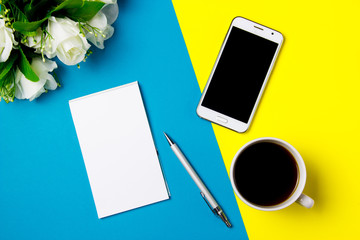 Smartphone, notepad and cup of coffee on a yellow and blue art background. Top view.