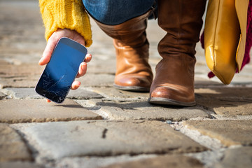 Woman picking up broken smartphone with cracked touch screen on the street