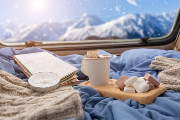 A cup of hot coffee with marshmallow near the window in the caravan camping car in the winter...