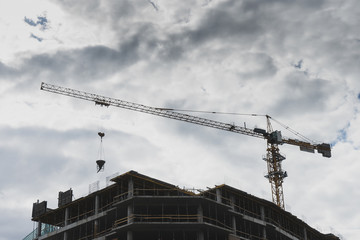 Building under construction against white cloudy sky. Big crane at the top at the time of work. Bottom view. Copy space.