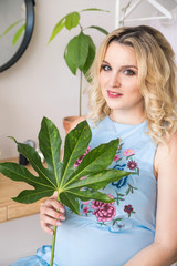 pregnant blonde girl holding a plant with large green leaves