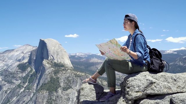asian elegant woman backpacker tourist in hat sit with map on rock on mountain top. relax female hiker searching way road adventure in half dome trail yosemite. young girl traveler with backpack