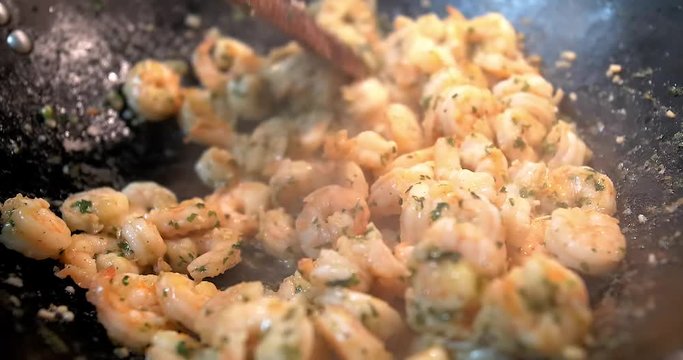 Slow zoom in, close up shot of shrimps being cooked with garlic and parsley while moving them with a wood spoon.