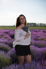 Beautiful woman with long hair, tattoos and a skirt. Cute girl holding a fragrant bouquet. Girl standing in the field among colorful, blooming lavender flowers in the summer in the countryside.